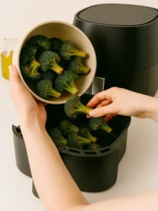 Broccoli florets being poured into an air fryer basket for cooking
