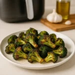 Crispy air fryer broccoli on white plate with golden edges, served on clean kitchen counter with air fryer in background"